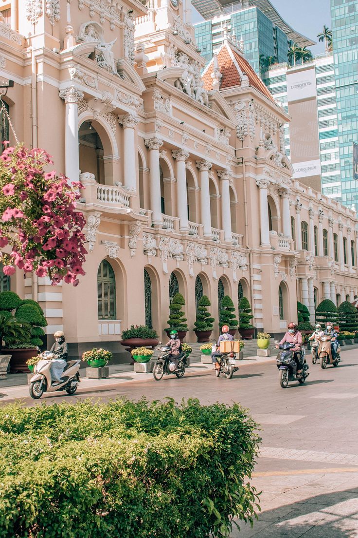 people riding motorcycles down the street in front of a large building