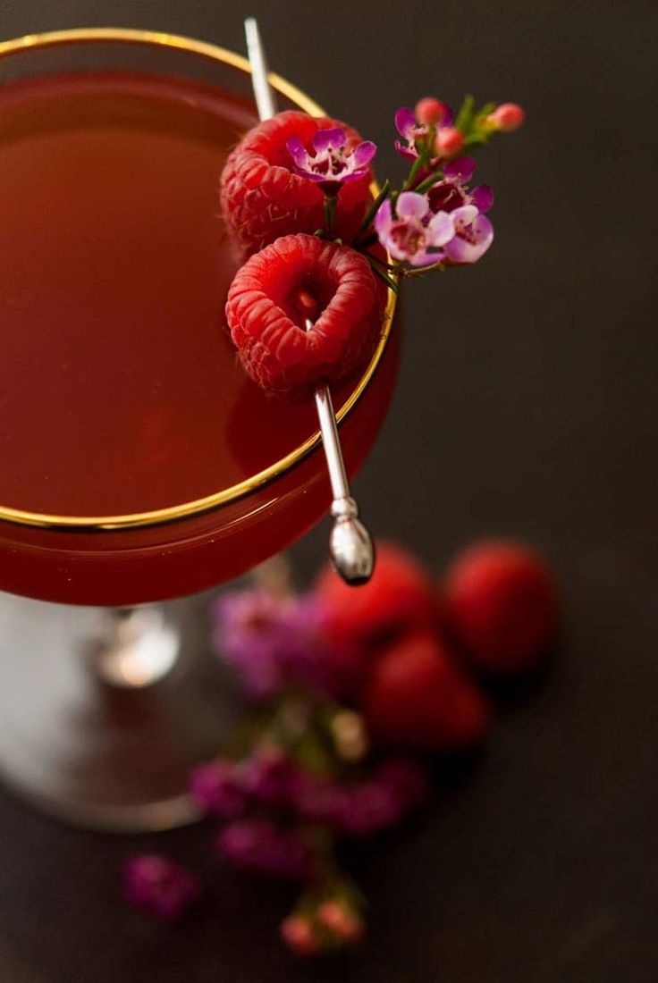 a close up of a cocktail with raspberries on the rim and garnish