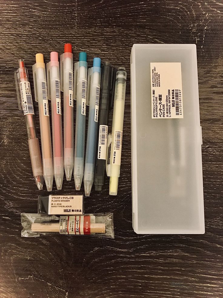 several markers and pens are sitting in a plastic container on a wooden table next to an empty package