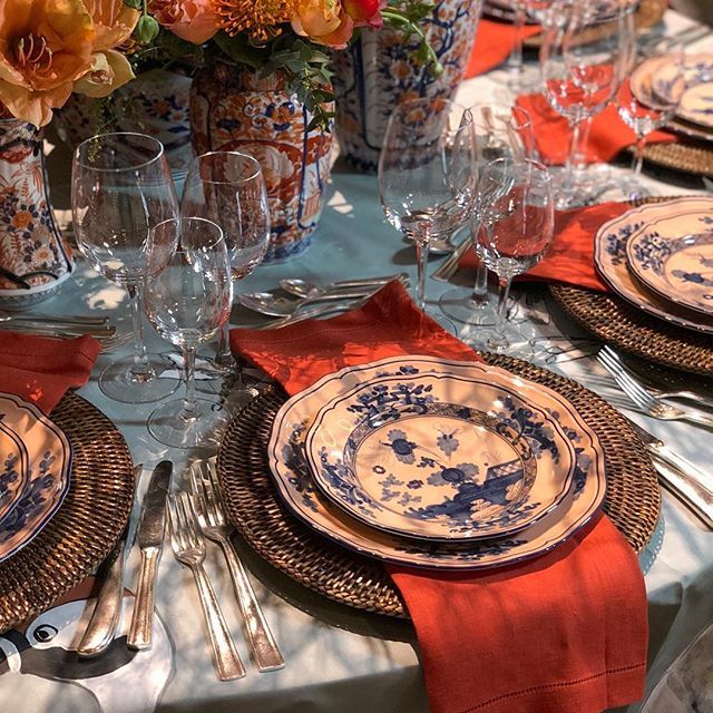 the table is set with plates, silverware and orange flowers in vases on it