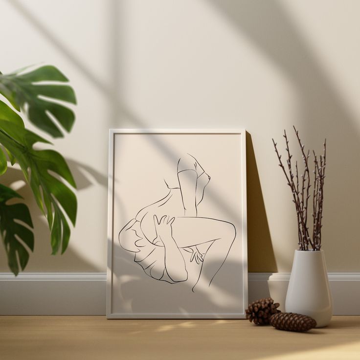 a white vase sitting on top of a wooden table next to a framed artwork piece