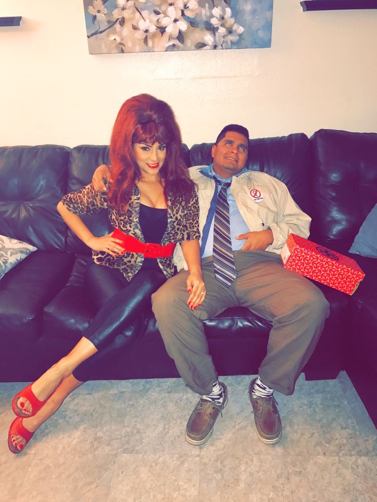 a man and woman sitting on a black couch with red ties around their ankles, posing for the camera