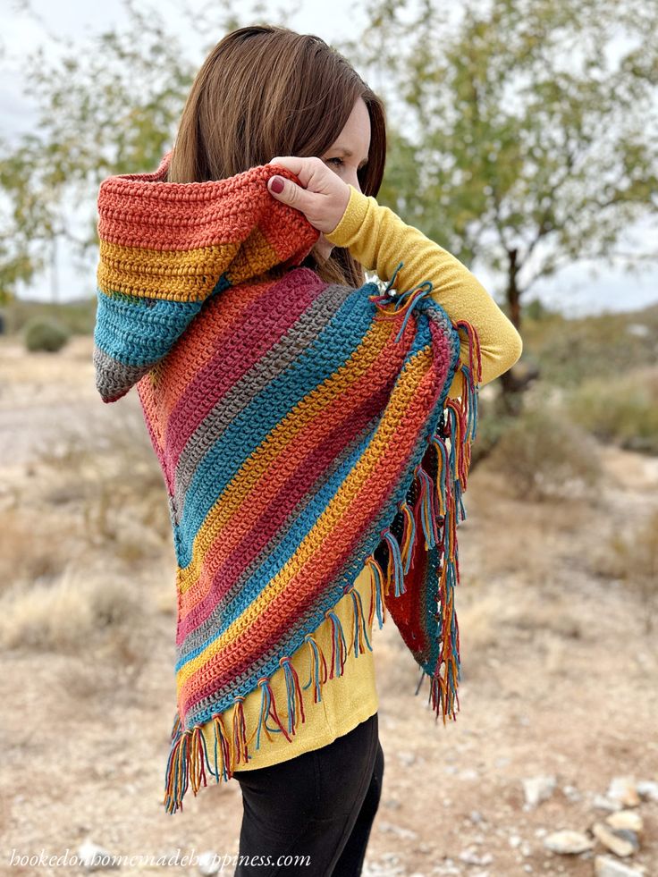 a woman wearing a multicolored crocheted shawl in the middle of nowhere