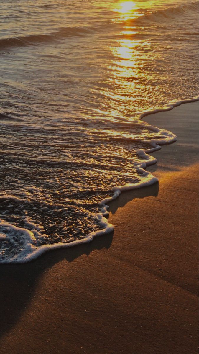 the sun is setting over the ocean with waves coming in on the sand and water