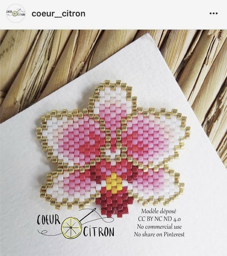 a card with a flower made out of small beads on top of white paper next to a wooden background