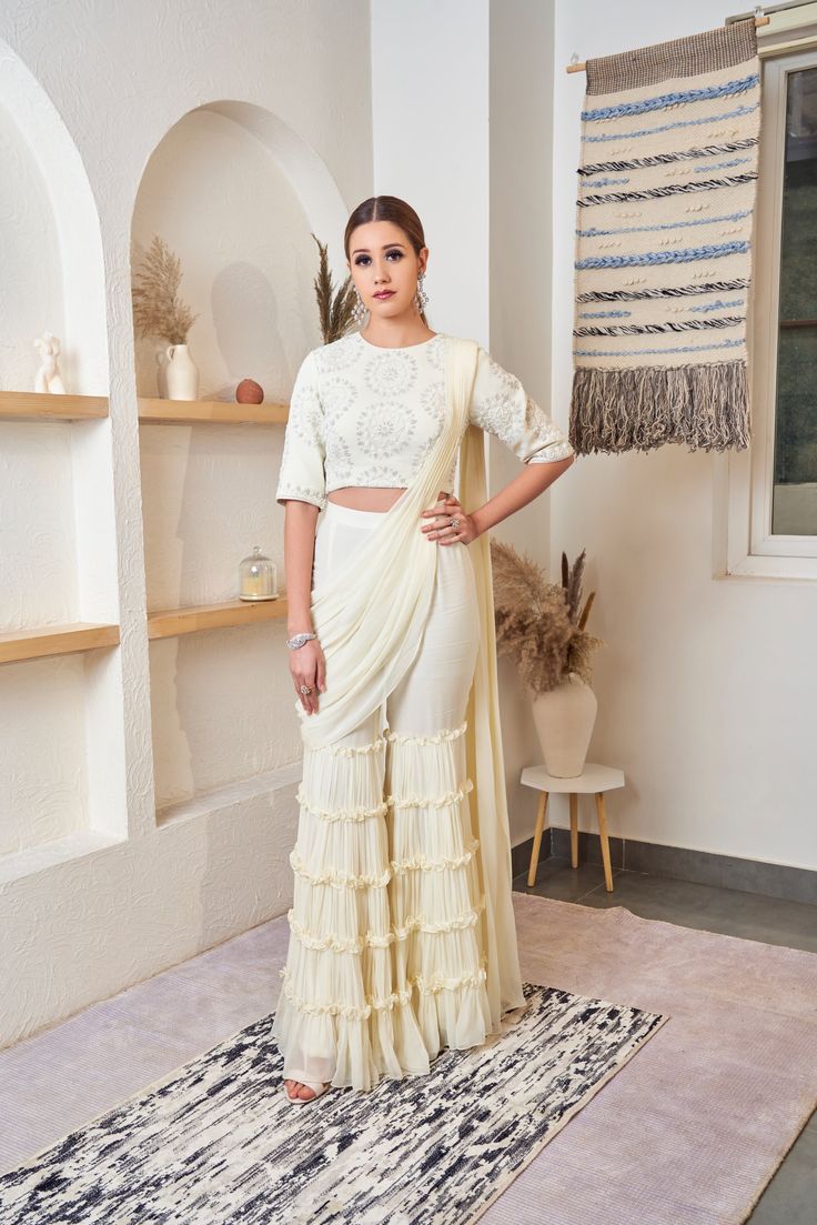 The off-white Sharara saree is made of georgette. The ensemble is etched with frills and scintillating details, it radiates elegance and class. Delivery Period: 2-3 weeks Traditional Pre-draped Off White Saree With Sheer Dupatta, Off White Pre-draped Saree With Sheer Dupatta, Designer Bollywood Pre-draped Saree In Off White, Cream Georgette Sharara For Reception, Designer Georgette Cream Pre-draped Saree, Off White Georgette Pre-draped Saree For Reception, Elegant White Designer Pre-draped Saree, Festive Off-white Georgette Sharara, Elegant White Pre-draped Saree For Eid