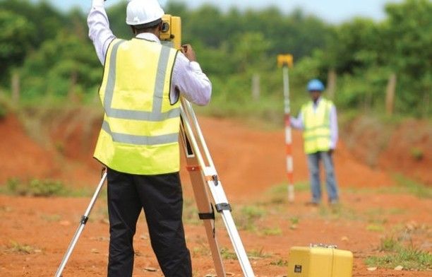 two men in yellow vests and hard hats standing on a dirt road with construction equipment