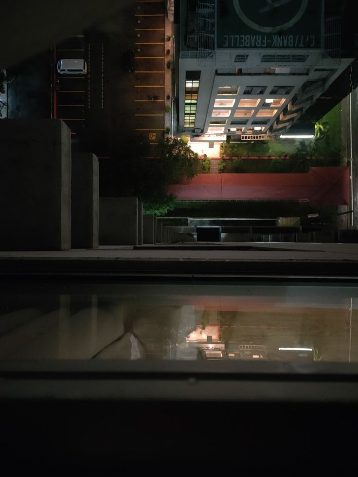 the reflection of a building at night with lights on and buildings in the back ground