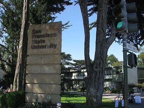 a traffic light sitting next to a large sign on the side of a road in front of some trees