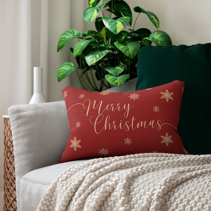 a christmas pillow sitting on top of a couch next to a green potted plant