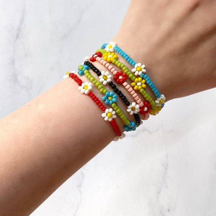 a woman's arm with four bracelets on it, one is multicolored and the other has white flowers