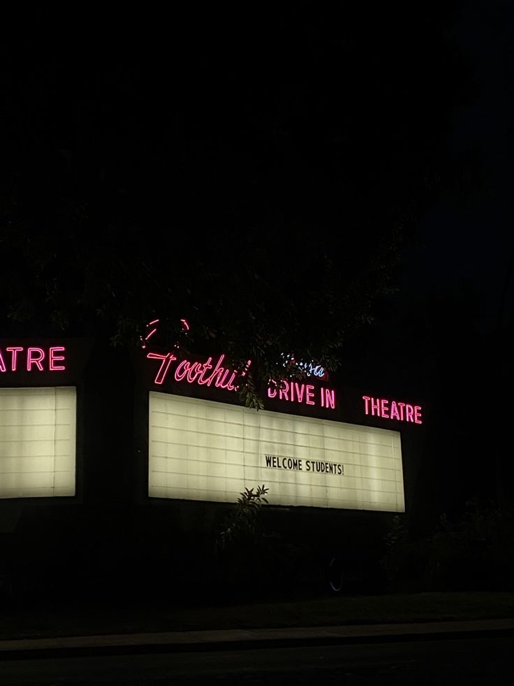 two large lighted signs on the side of a building in front of trees at night