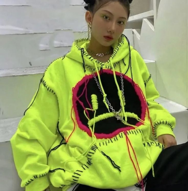 a woman sitting on top of a white bench wearing a neon green sweatshirt and black pants