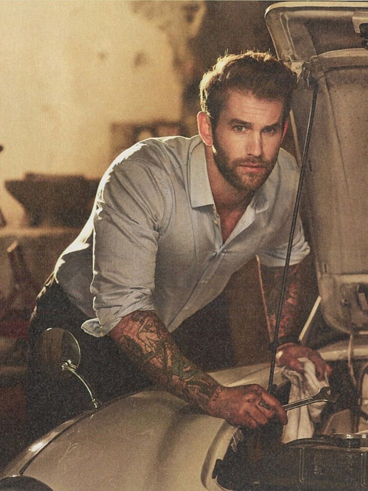 a man leaning on the hood of a car with his hands in the engine compartment