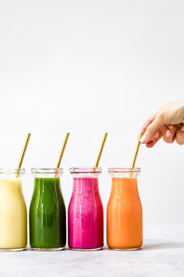 four different colored smoothies in small glass jars with gold straws and one being dipped