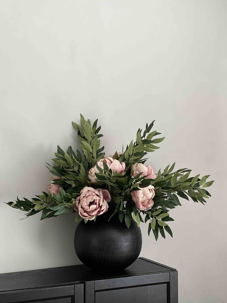 a black vase filled with pink flowers on top of a dresser