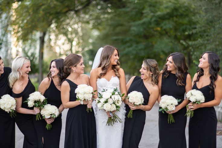 a group of women standing next to each other in black dresses holding bouquets and smiling