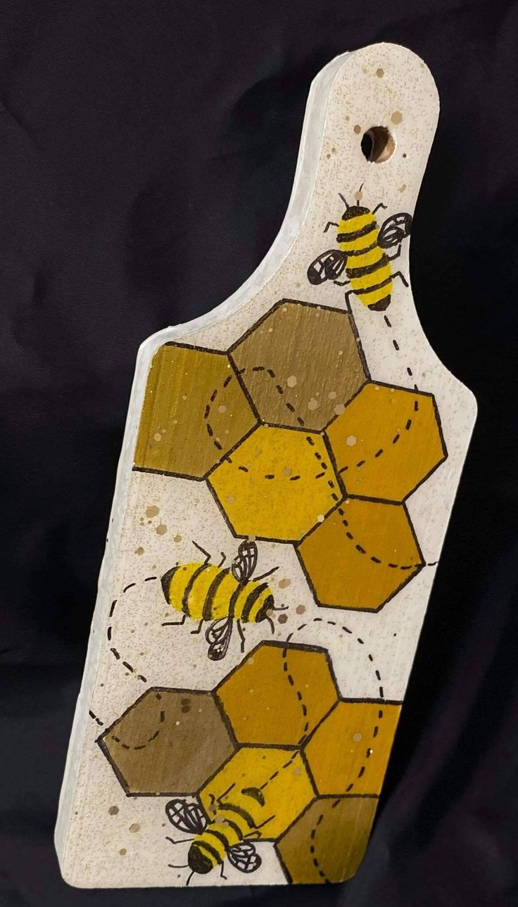 a wooden cutting board with bees painted on it's sides and yellow honeycombs