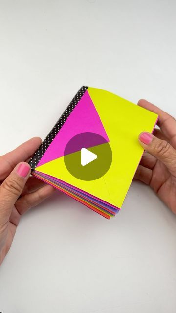 a person holding a stack of brightly colored papers with a video playing button on it