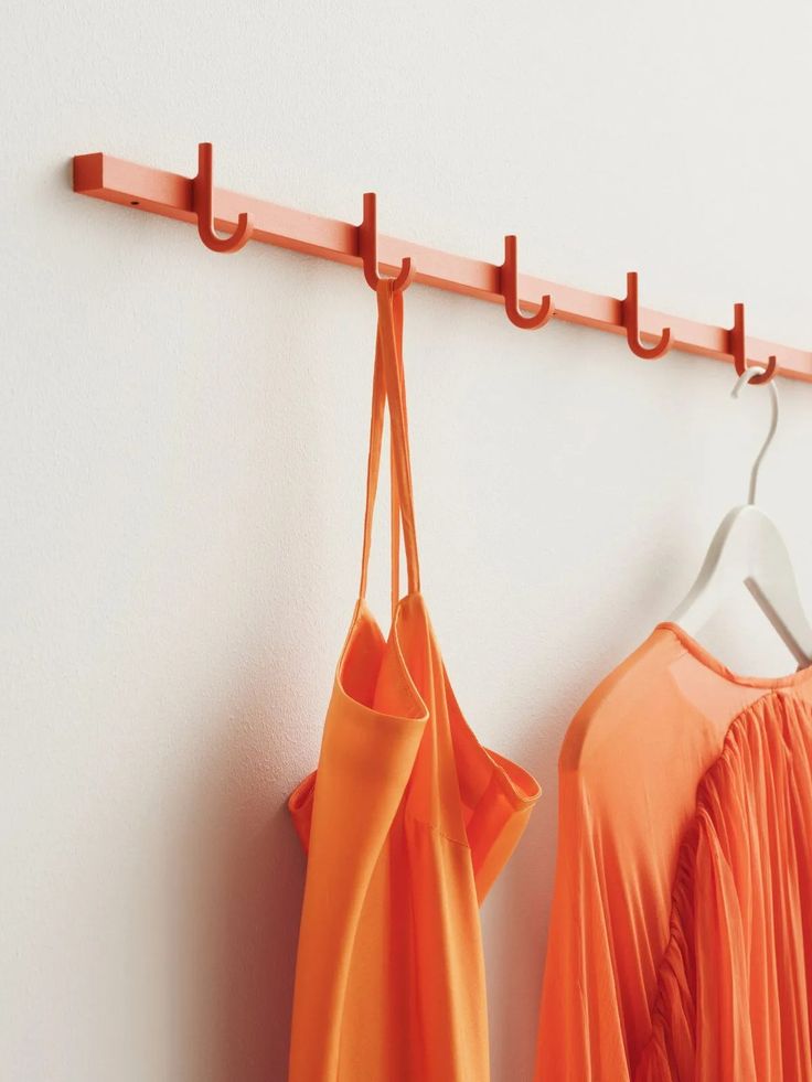 an orange dress hanging on a wall next to a hanger with two bags attached