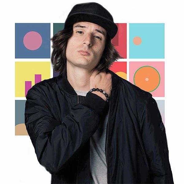 a young man wearing a black hat and jacket with his hands on his chest, standing in front of colorful squares