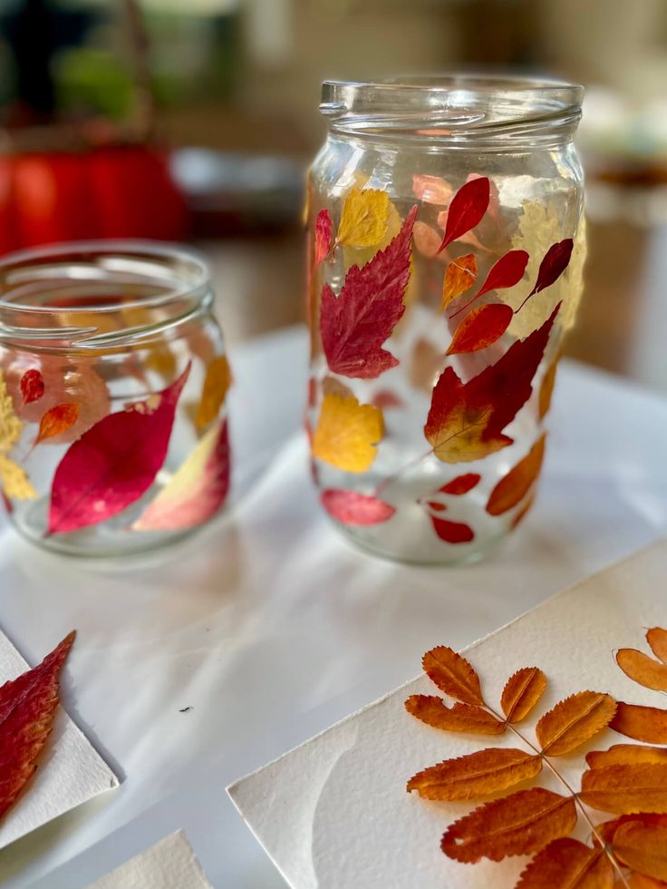 two jars with leaves painted on them are sitting on a table next to paper towels