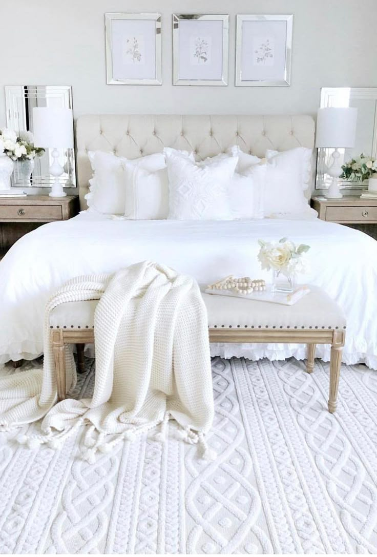 a white bed with pillows and blankets on top of it, next to two nightstands