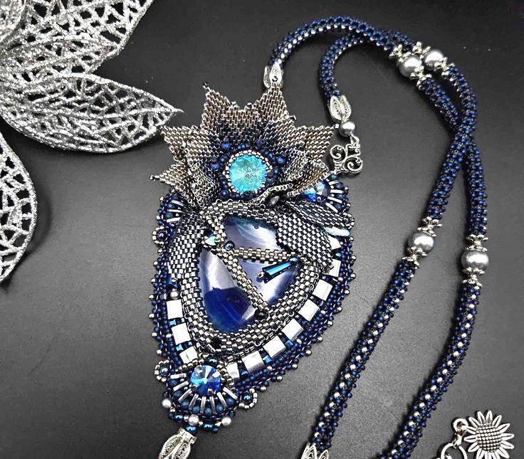 an elaborate necklace with blue beads and silver accents on a black surface next to a leaf shaped brooch