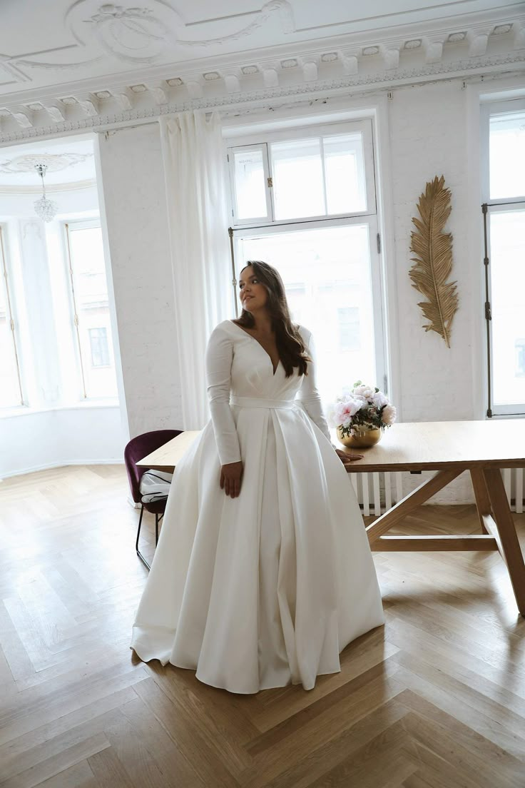 a woman in a white wedding dress sitting on a wooden floor next to a table