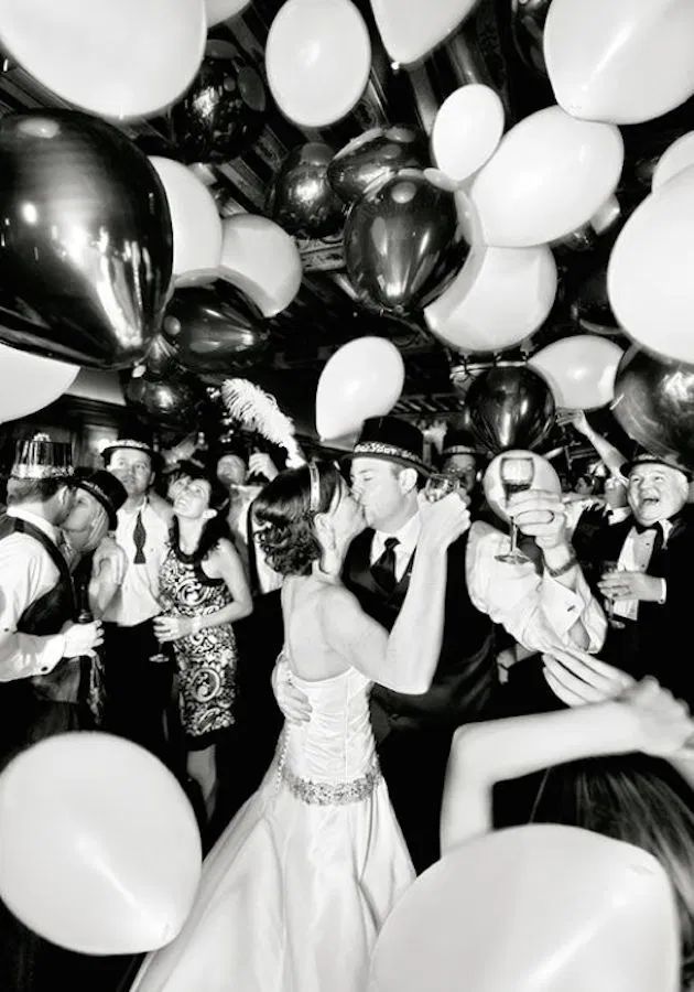 black and white photo of bride and groom kissing surrounded by balloons at their wedding reception