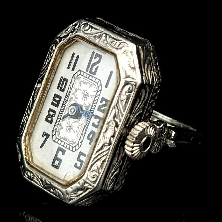 Presenting a remarkable Art Deco era ring watch convertible to wrist watch, a true novelty piece that encapsulates the elegance and ingenuity of the past. Crafted in 14k white gold, this antique/vintage piece features a double shank that cleverly opens up into watch lugs, allowing for the watch to be converted into a wrist watch with the addition of a cord strap (not included). The white dial adorned with Arabic numerals and beautiful floral accents sits within an exquisitely engraved case, a te Luxury Art Deco Watch With Manual Winding, Antique Platinum Jewelry And Watches For Evening, Timeless Collectible Jewelry With Round Dial, Timeless Engraved Watches For Anniversary, Antique Engraved Jewelry And Watches For Wedding, Antique Platinum Jewelry And Watches For Wedding, Timeless Hallmarked Jewelry And Watches For Wedding, Timeless Engraved Jewelry And Watches For Wedding, Antique Platinum Wedding Jewelry And Watches