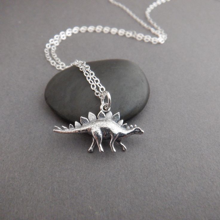 a small silver dinosaur necklace sitting on top of a black piece of rock next to a chain