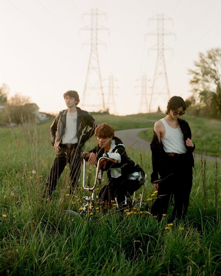 three people standing in the grass with one holding a bike