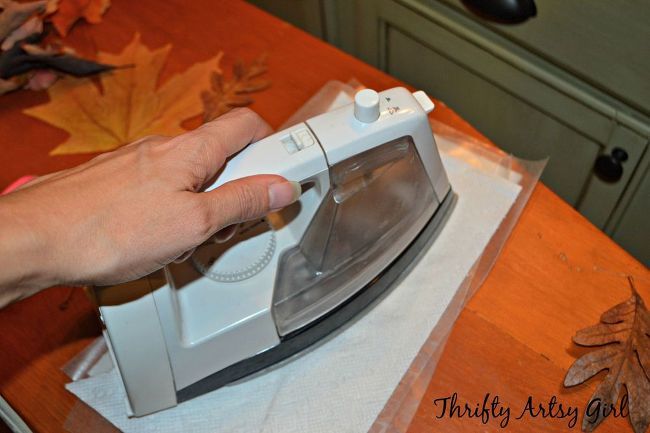 a person is using an iron on top of a table with autumn leaves around it