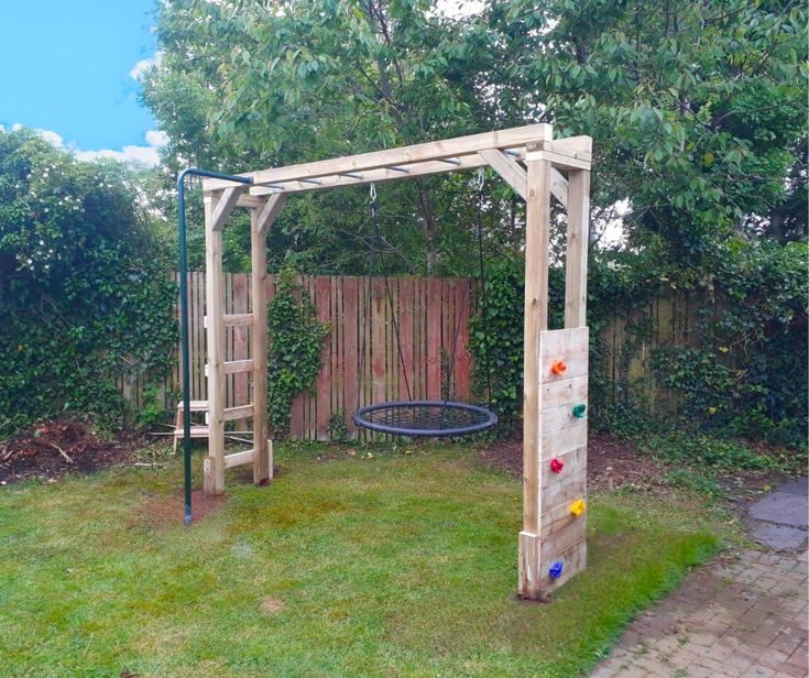 a backyard with a swing set and swings in the grass next to a wooden fence