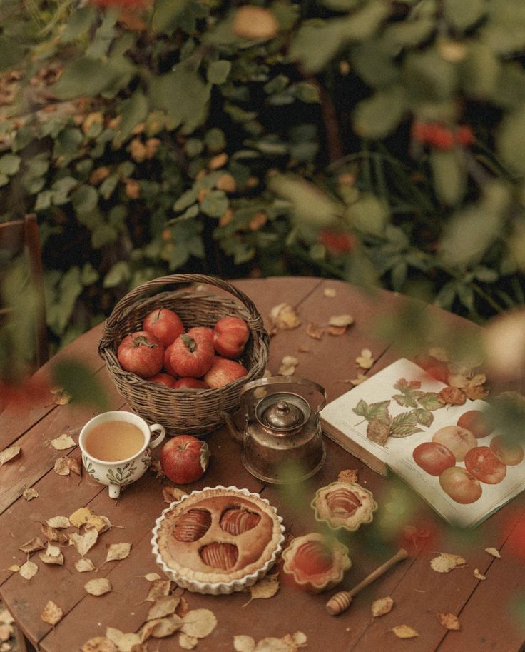 a table topped with apples next to a basket of leaves and a cup of tea