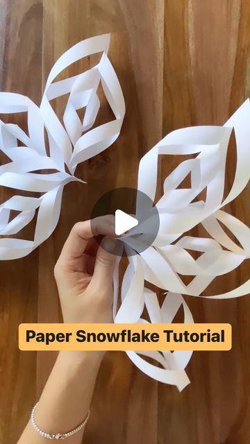 someone is making paper snowflakes out of white paper on a wooden table