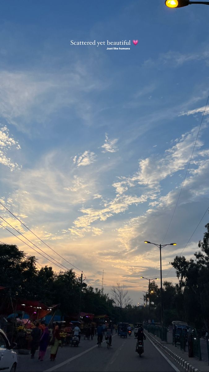 people are riding bikes down the street under a traffic light at sunset or dawn with clouds in the sky