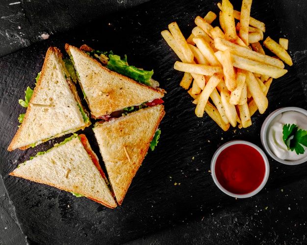 a sandwich and french fries on a black slate board with ketchup, mayonnaise and sauce