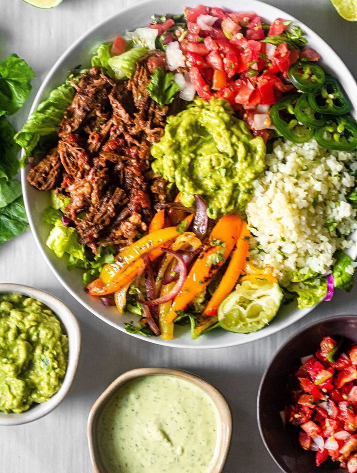 a large bowl filled with meat and vegetables next to bowls of guacamole