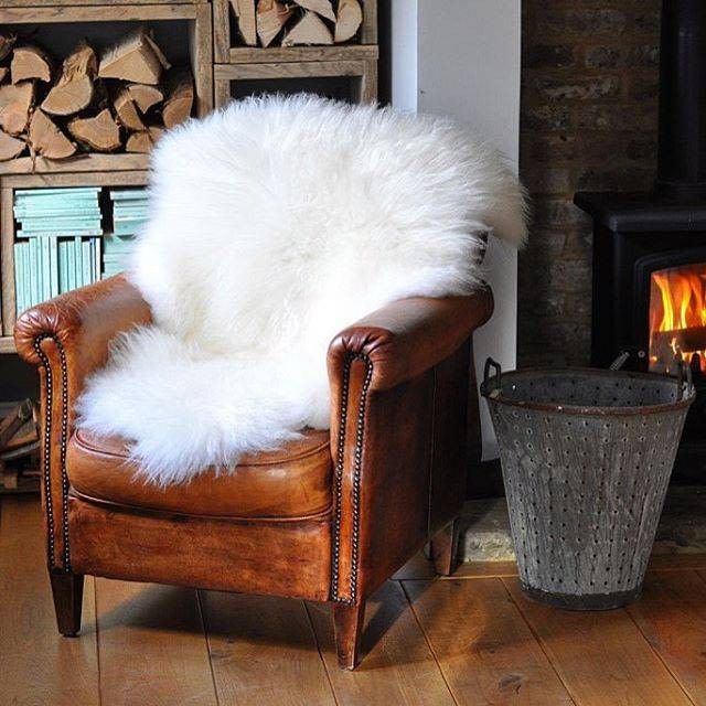 a chair with a white fur on it in front of a fire place and logs