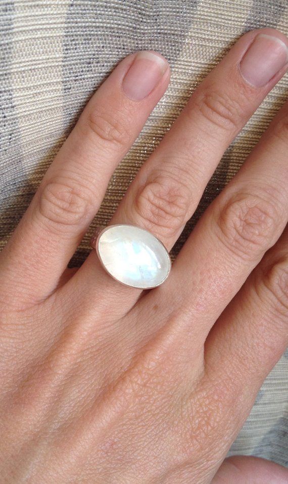 An elegant crystal white large oval Rainbow Moonstone has been set in sterling silver. The ring band is handmade from a fancy patterned sterling silver thick wire. This moonstone is pearly white and shines on its own with hues of pink, blue, and even orange. The luminescent quality of the moonstone makes this ring beautifully unique and elegant. The stone is 13mm x 18mm in size with a height of about 8mm. This moonstone can be set vertically (North to South) rather than horizontally as shown. Ju Modern Oval Cabochon Moonstone Ring, Modern Oval Moonstone Ring With Large Stone, Handmade Oval Moonstone Ring In Modern Style, Modern Handmade Oval Moonstone Ring, Handmade Modern Oval Moonstone Ring, Minimalist White Oval Jewelry, Large Oval Moonstone Ring, Modern Adjustable Oval Moonstone Ring, Minimalist Handmade White Moonstone Ring