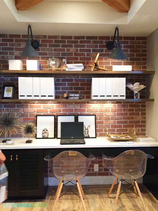 two clear chairs sit in front of a brick wall with shelves above it and below them