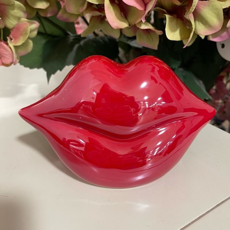 a close up of a red lip shaped bowl on a table with flowers in the background