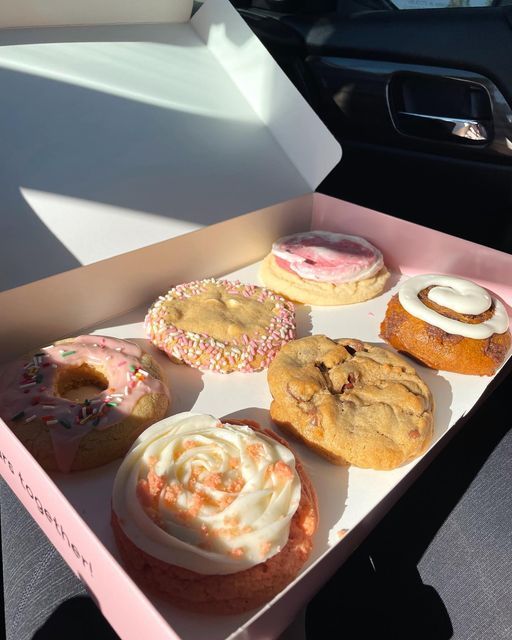 a pink box filled with lots of different types of doughnuts on top of a table