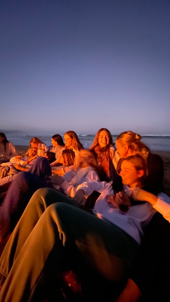 a group of people sitting next to each other on top of a beach at night