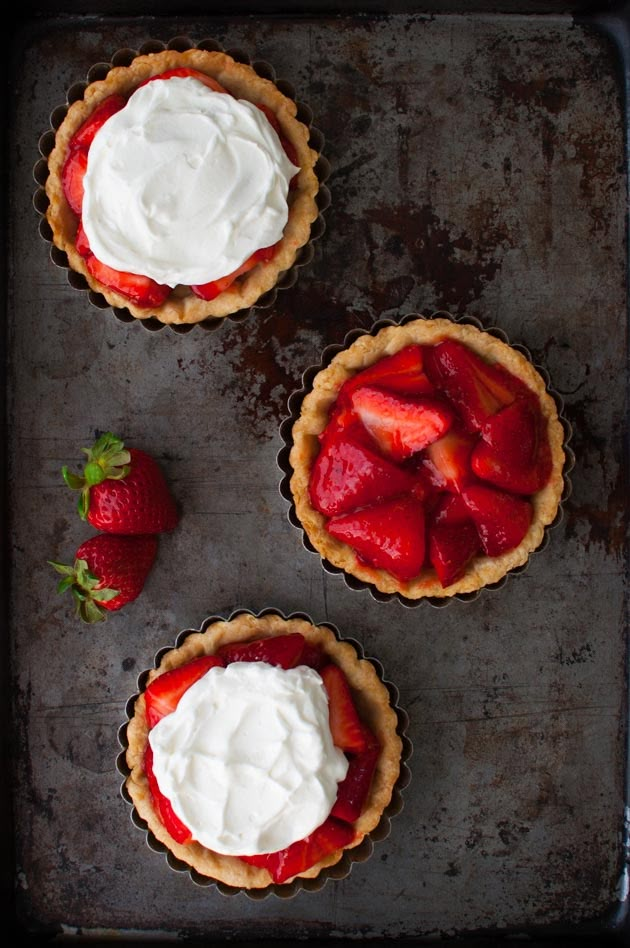 three pies with strawberries and whipped cream on top sitting on a baking sheet