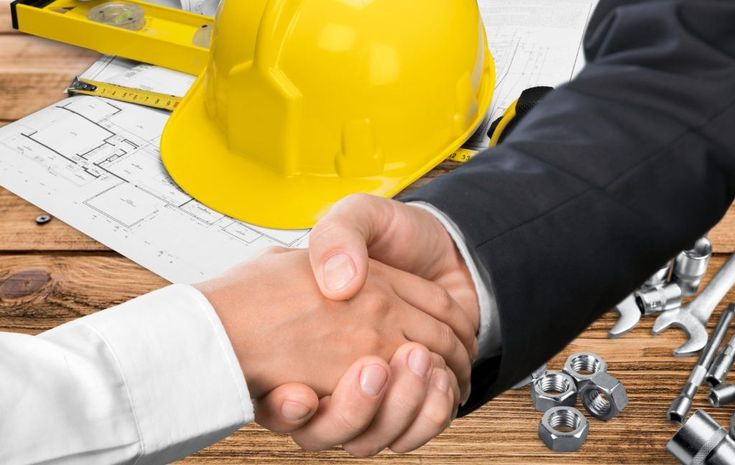 two people shaking hands over construction plans and tools