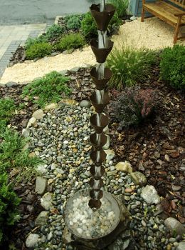 a fountain in the middle of a garden with rocks and gravel around it, next to a bench