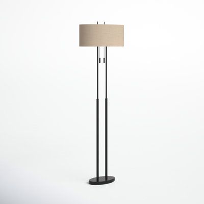 a black floor lamp with a beige shade on the top, and a white background